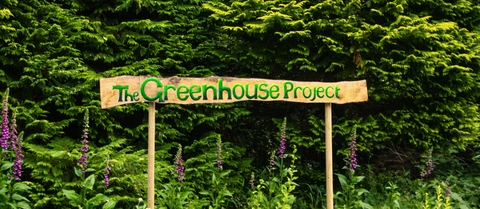 A wooden handpainted sign saying 'The Greenhouse project'