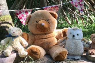 Three teddy bears and a cuddly owl toy sitting together in a woodland