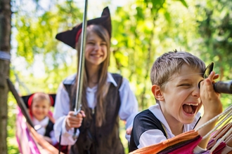 Children dressed up as pirates in a hammock within a woodland