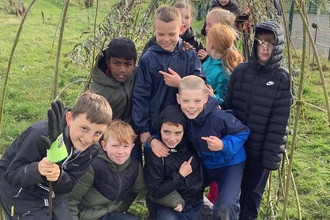 A group of children in a group underneath their handmade willow archway