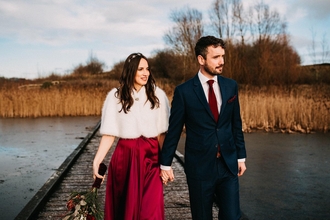 A bride and groom walk along the boardwalk over a frozen Meadow Lake