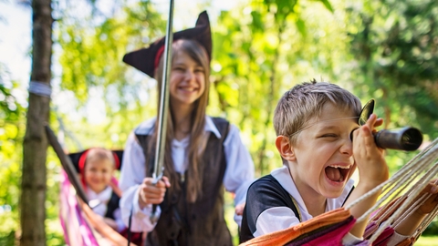 Children dressed up as pirates in a hammock within a woodland