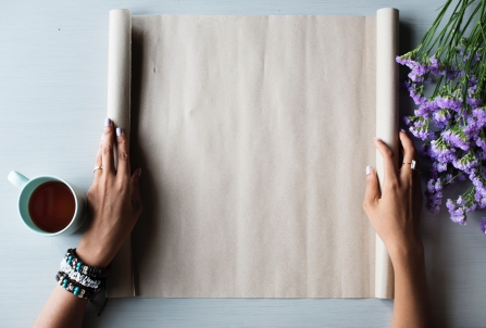 A woman laying out brown paper wrapping next to a cup of coffee on a table