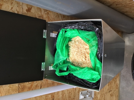 A bin bag full of sawdust sitting in a silver tub with the lid standing open