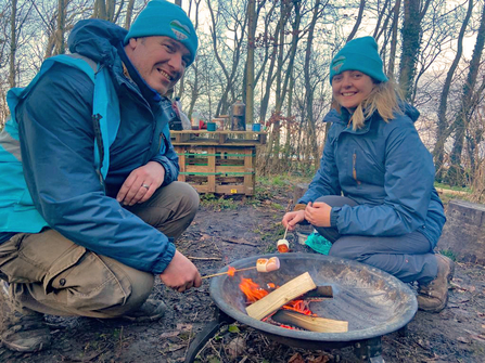 Two people crouched by a fire bowl toasting marshmallows