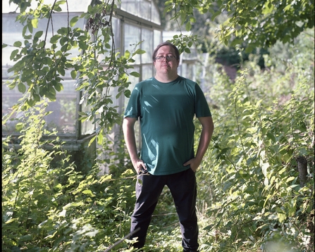 A man in a green t-shirt standing in front of a greenhouse