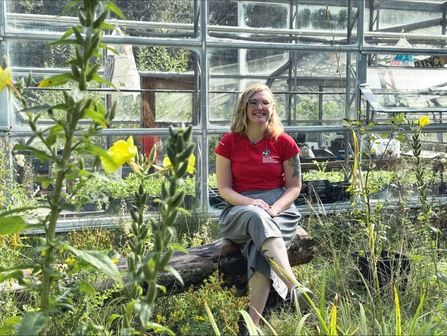 A blonde woman sitting outside a greenhouse in the sun