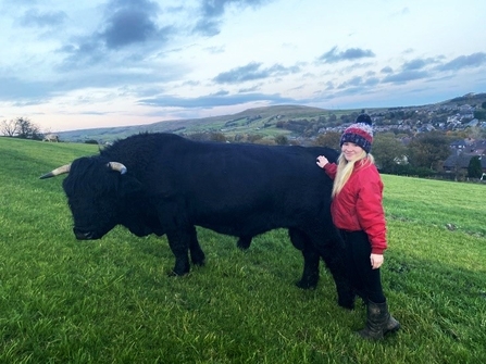 A young woman with blonde hair wearing a bobble hat and standing next to a black bull