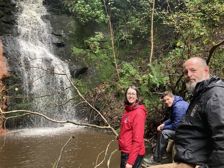 3 people smiling next to a waterfall