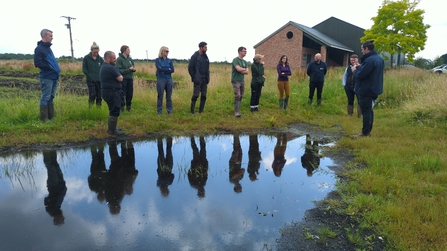 Group of people next to a pond in a green field