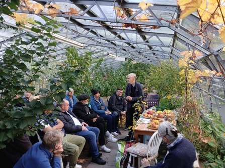 A group of people n a greenhouse with a table of apples