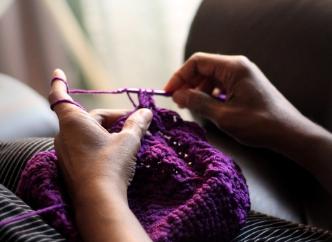 Woman sitting and knitting with purple thread