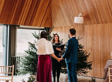 A bride and groom holding hands standing in front of their wedding officiant in the Meadow Lake Suite